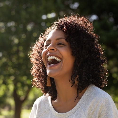 Woman with curly hair and gray blouse laughing outdoors