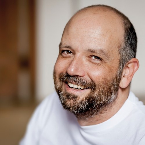 Older man with short beard and white tee shirt smiling