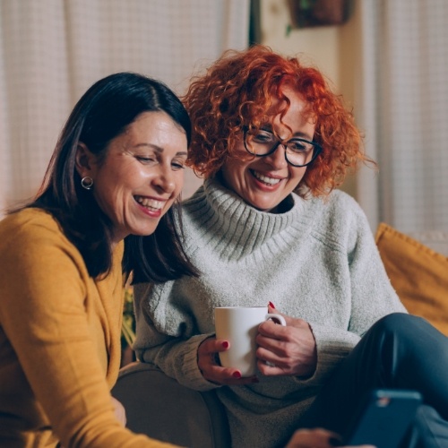 Two smiling women on couch looking at something out of frame together