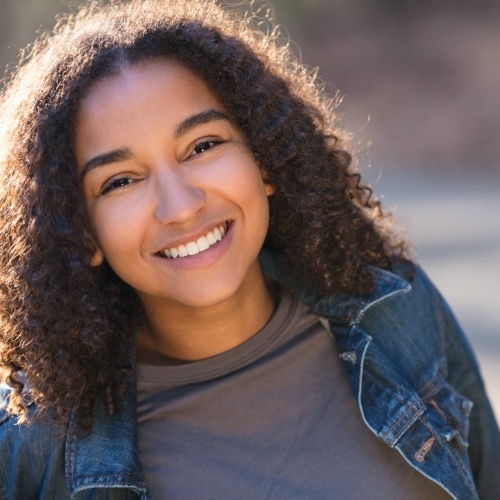 Young woman with curly hair and denim jacket grinning