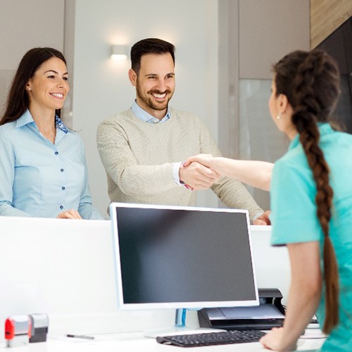 Smiling male patient shaking hands with dental receptionist