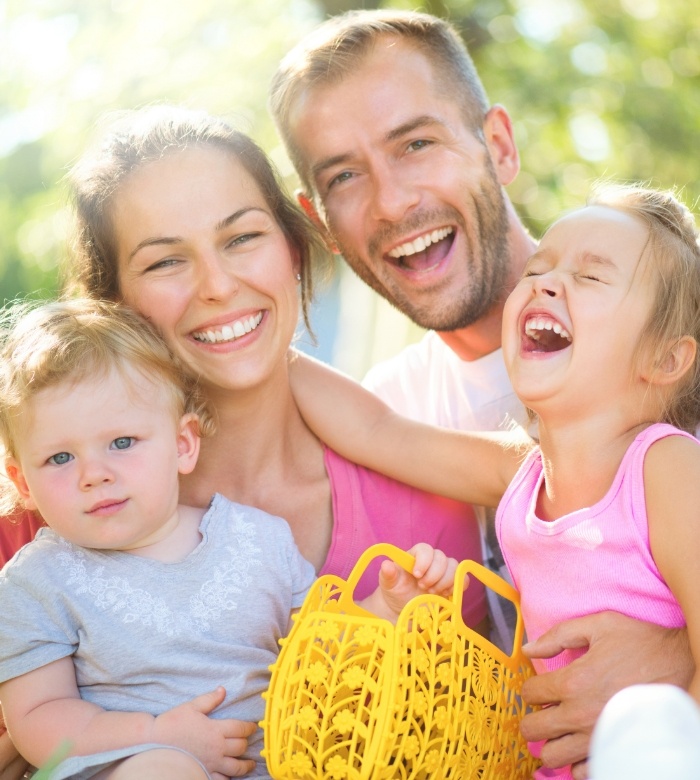 Laughing family of four laughing outdoors with a yellow basket