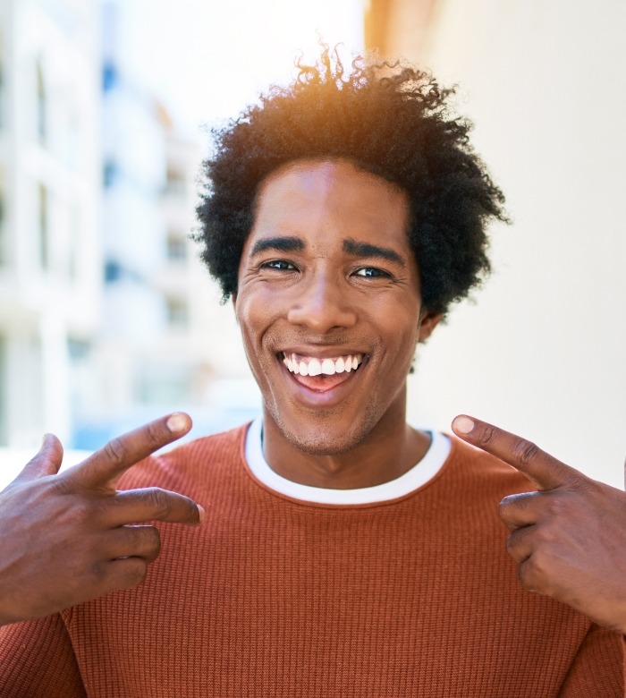 Man in orange sweater pointing to his smile after restorative dentistry in Norman