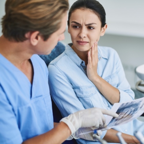 Woman holding her cheek in pain while talking to dentist about T M J treatment