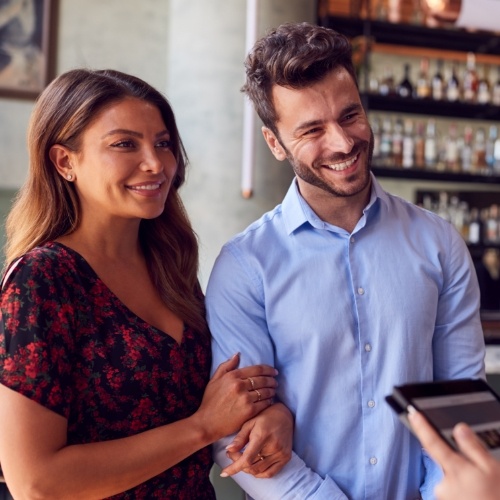 Woman holding man's arm while they pay at a restaurant