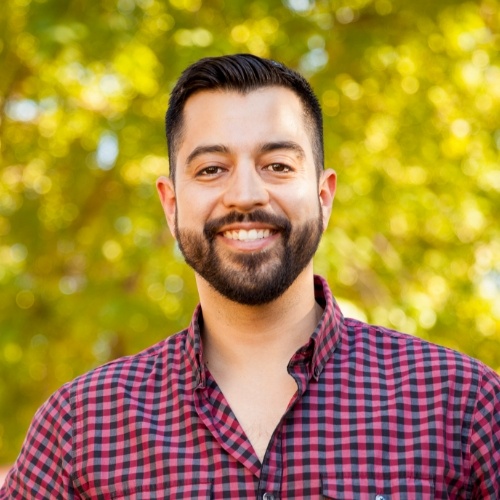 Man in red and black plaid shirt smiling outdoors