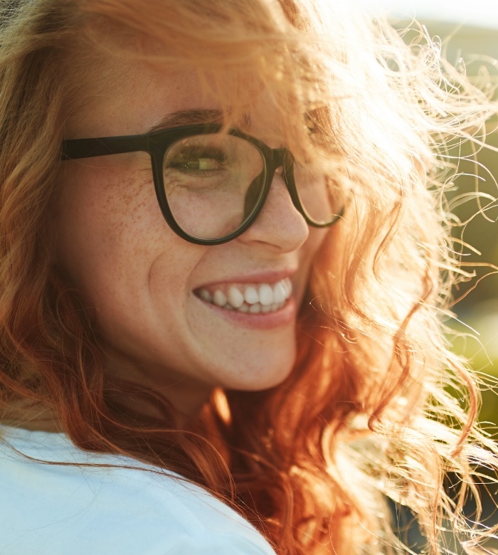 Young woman with red hair and freckles smiling outdoors with a dental bridge in Norman