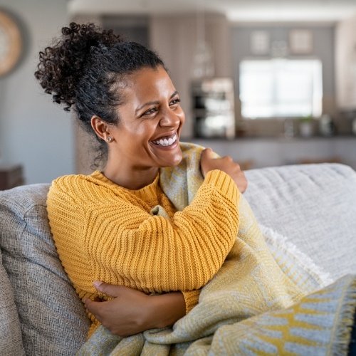 Woman in yellow sweater smiling while sitting on couch under a blanket