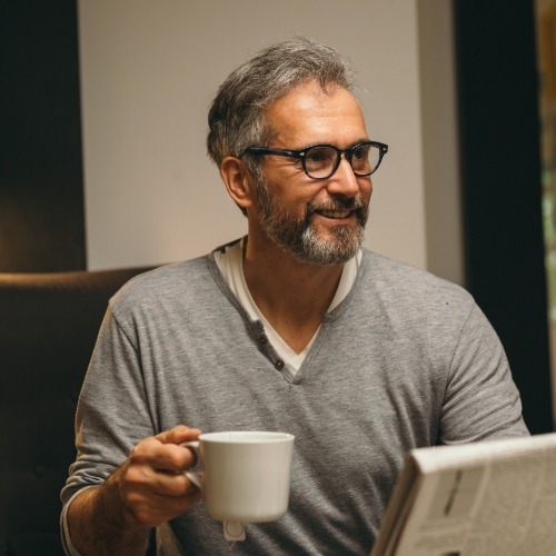 Man in gray sweater with glasses holding coffee mug