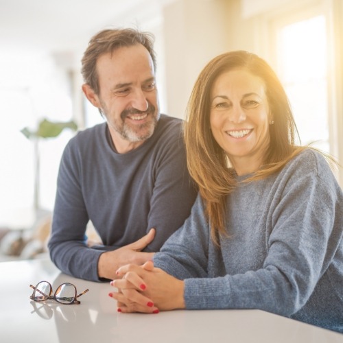 Man and woman smiling in their kitchen with sunlight coming through window on side