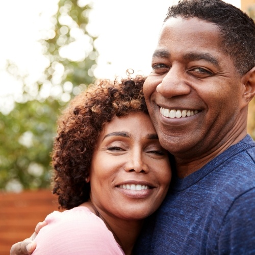 Woman resting her head on man's chest while smiling and standing outdoors