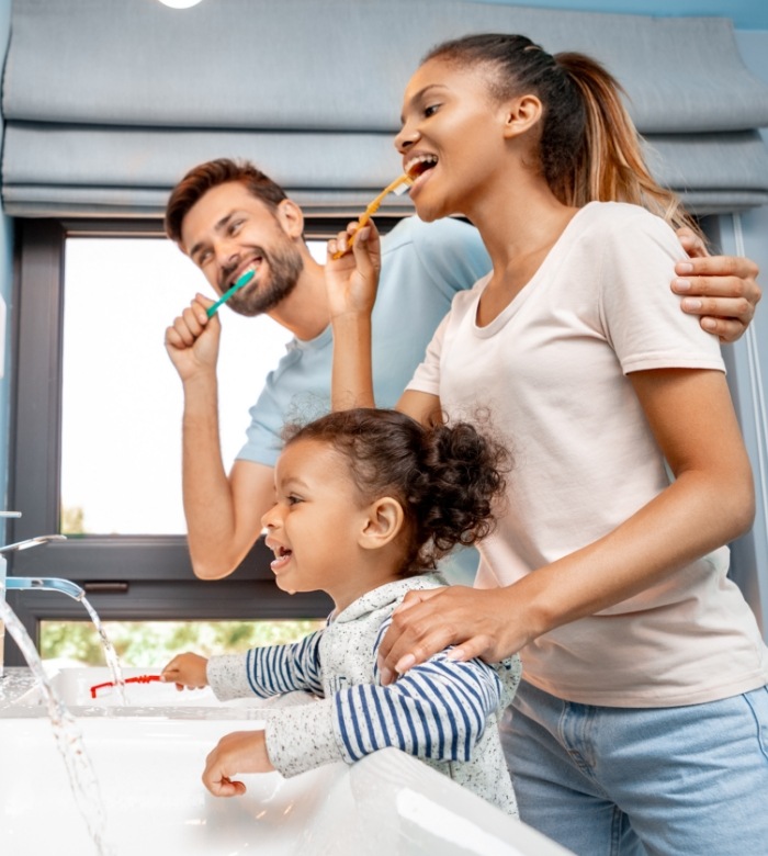 Mother father and young child brushing teeth together in front of mirror