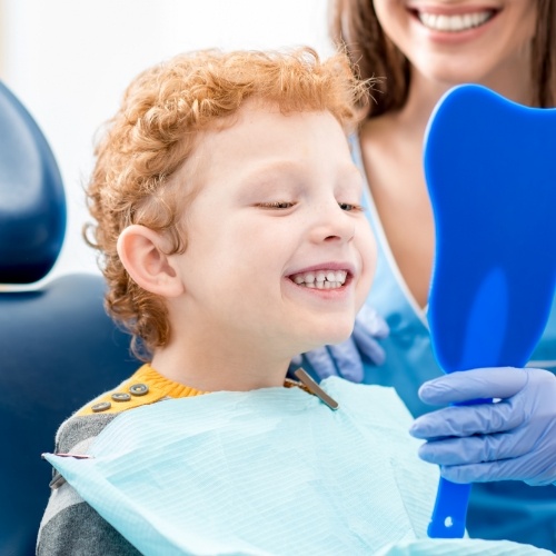 Young boy with curly hair seeing his smile in mirror during dental visit