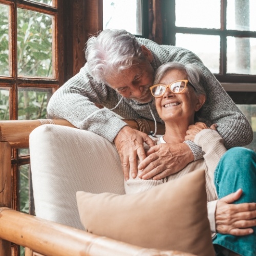 Man standing behind couch hugging woman sitting on couch