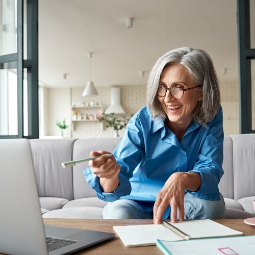 Woman holding pen while pointing at laptop on her desk