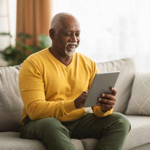Man in yellow shirt sitting on couch and using tablet