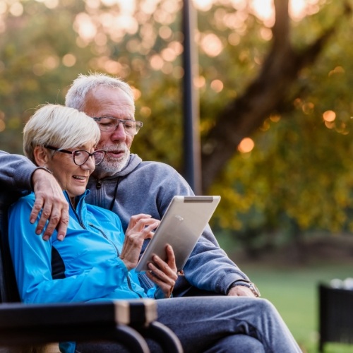 Older man and woman sitting on park bench looking at tablet together