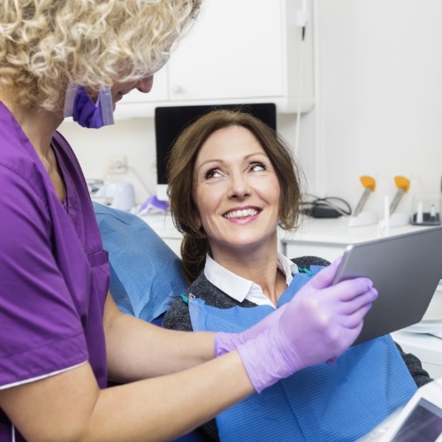 Woman in dental chair smiling as dental team member shows her a tablet screen