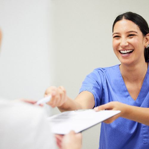 Dental assistant smiling while handing patient forms