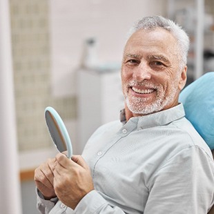 Senior man smiling in dental chair while holding handheld mirror