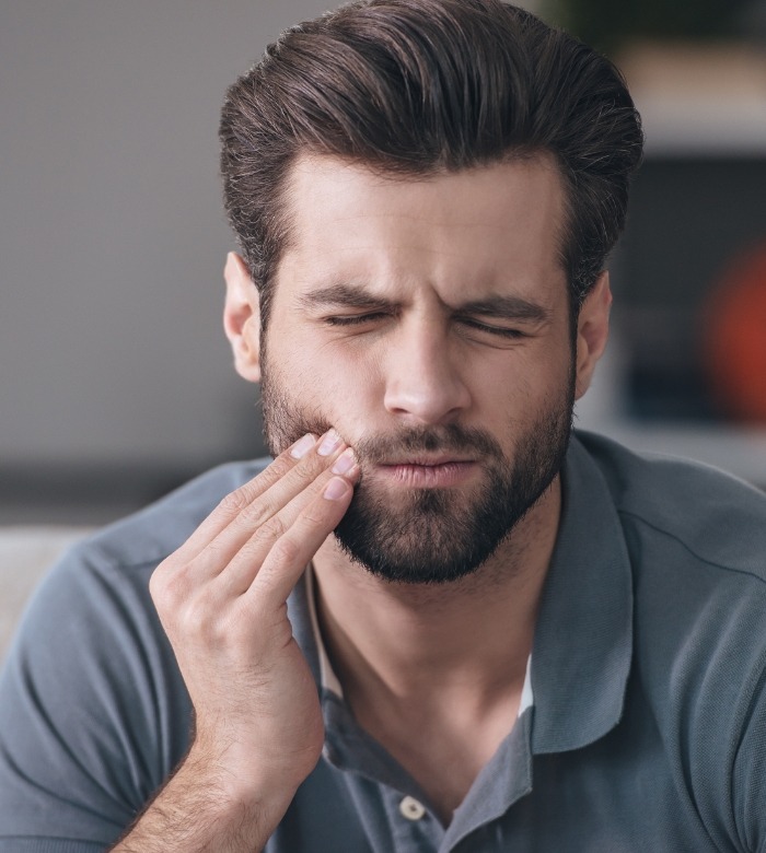 Man who needs emergency dentist in Norman holding cheek in pain