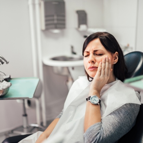 Woman in dental chair holding cheek in pain