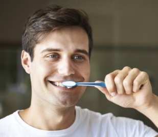 Man smiling while brushing his teeth