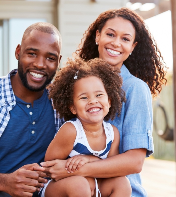 Family of three smiling outdoors after seeing cosmetic dentist in Norman