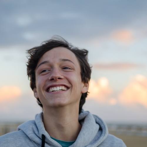 Smiling young man wearing gray hoodie on beach at sunset