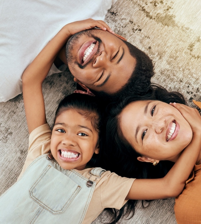 Mother father and young child lying on floor in circle with their heads touching