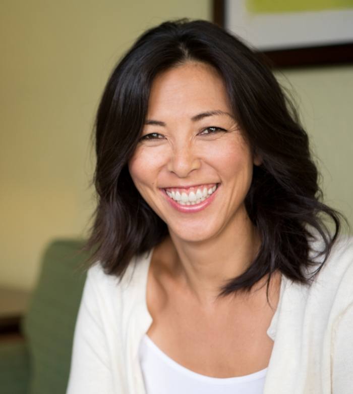 Woman in white blouse grinning after full mouth reconstruction in Norman