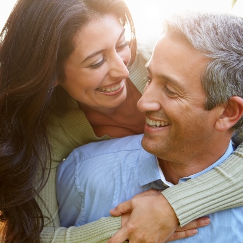 Man and woman smiling at each other outdoors while embracing
