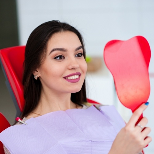 Young woman looking at her new smile in mirror after full mouth reconstruction