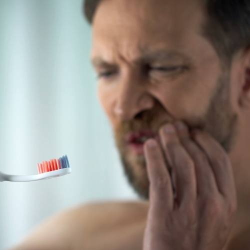 Man with bloodied toothbrush holding the side of his face in pain