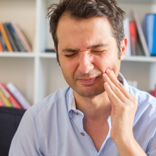 Man sitting on couch and holding his cheek in pain