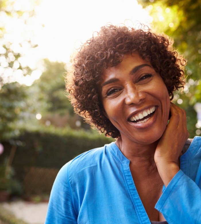 Woman in blue blouse smiling outdoors with implant dentures in Norman