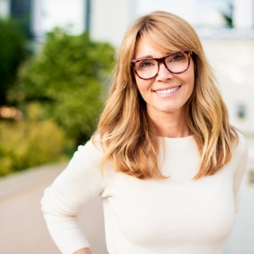 Woman with long blonde hair and glasses smiling outdoors