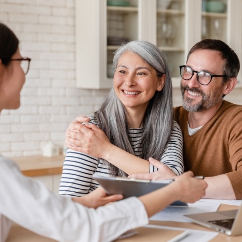 Man and woman at their kitchen table talking to a woman about the cost of implant dentures