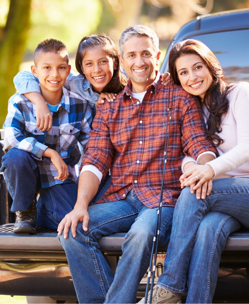 Smiling family of four sitting on bed of pickup truck
