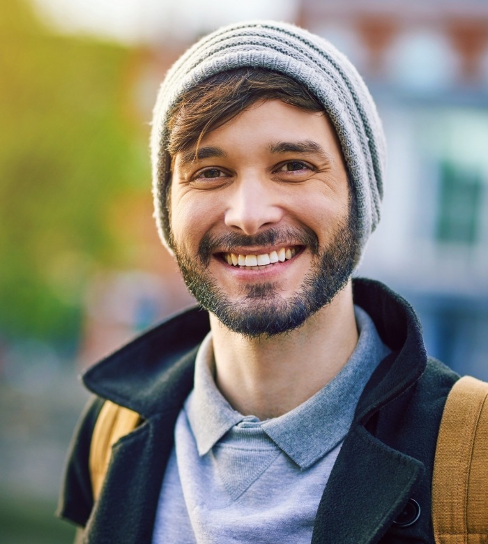 Young man in beanie smiling after replacing missing teeth in Norman