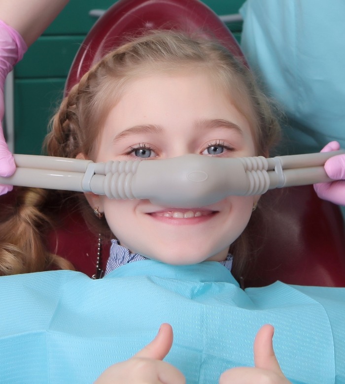 Young girl in dental chair giving thumbs up and wearing mask for nitrous oxide sedation in Norman