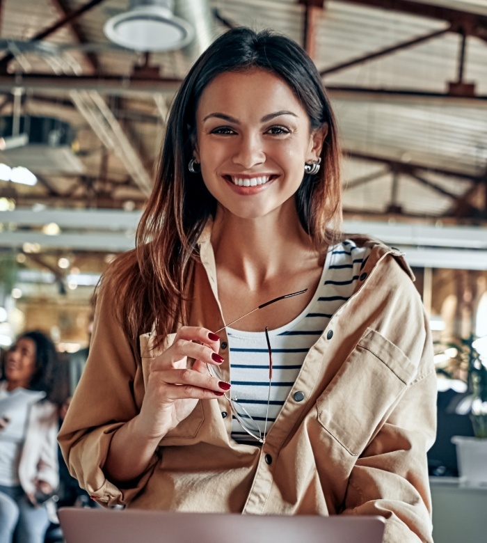 Smiling woman in an office holding her glasses after seeing sedation dentist in Norman