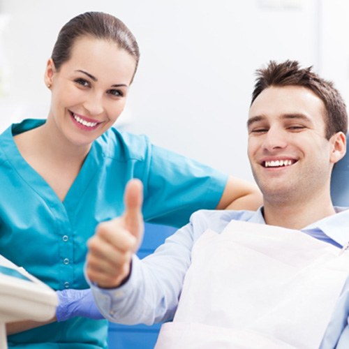 Smiling male patient giving thumbs up with dental assistant