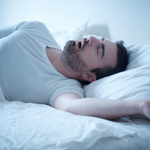 Man in white tee shirt sleeping in bed with mouth open