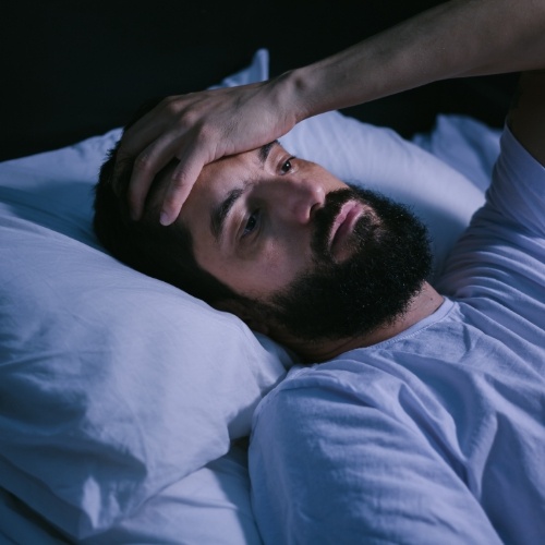 Man lying in bed with hand on his forehead looking worried