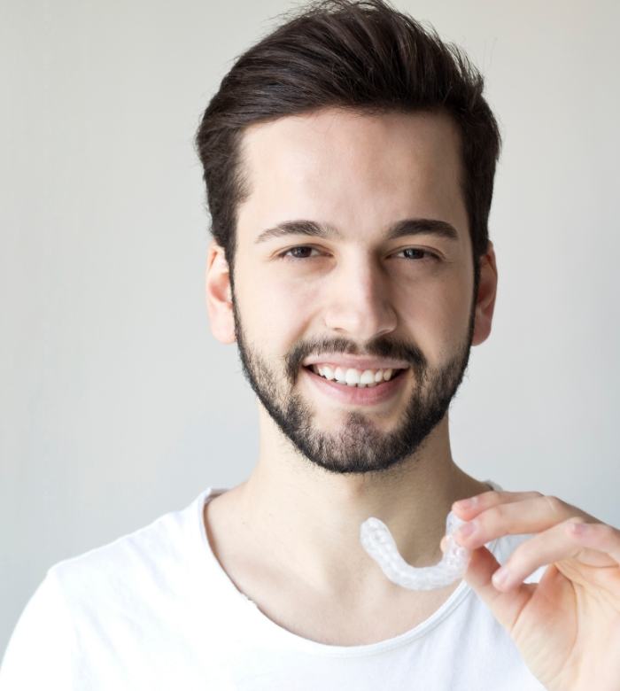 Young man with short beard holding a nightguard for teeth grinding treatment in Norman