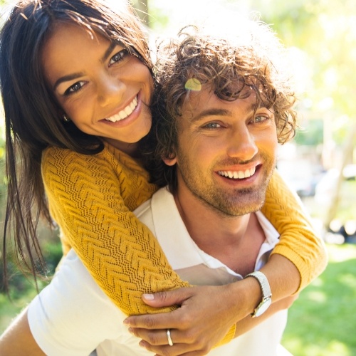 Smiling young man giving young woman piggyback ride