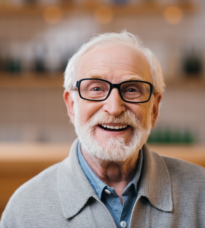 Senior man with glasses smiling after tooth extractions in Norman