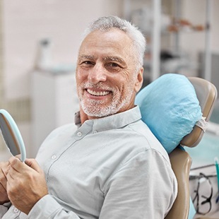 Senior man smiling while holding handheld mirror