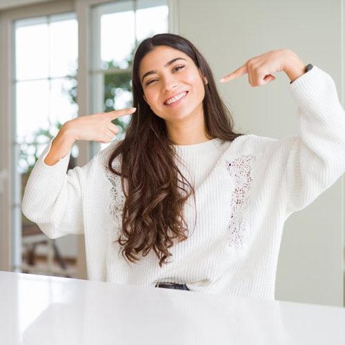 Woman smiling in her kitchen and pointing at her teeth